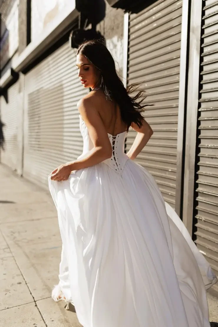 Model is wearing a scoop neck spaghetti strap wedding dress with a full gathered skirt 