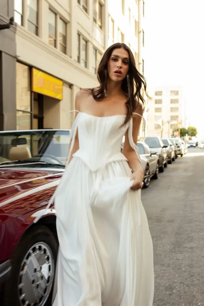 Model is wearing a scoop neck spaghetti strap wedding dress with a full gathered skirt 