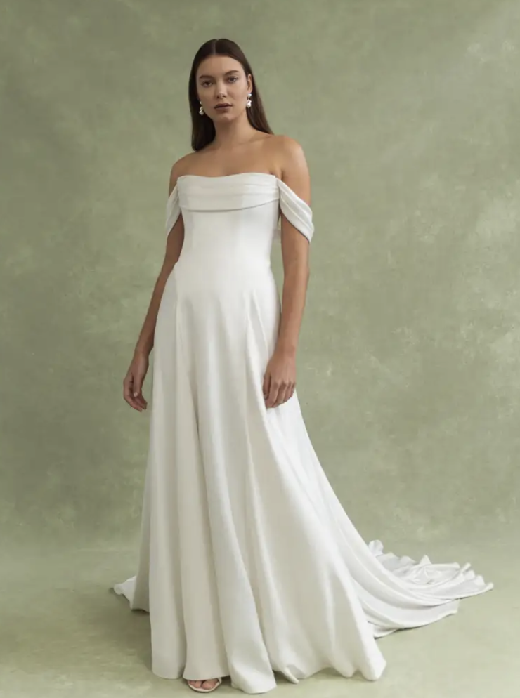 Model is wearing the Jenny by Jenny Yoo Lee gown, featuring an off-the-shoulder neckline, ruched bodice, dropped waist, and a clean A-line silhouette.