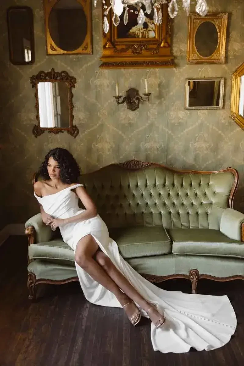 model is wearing an off the shoulder wedding dress with a slit