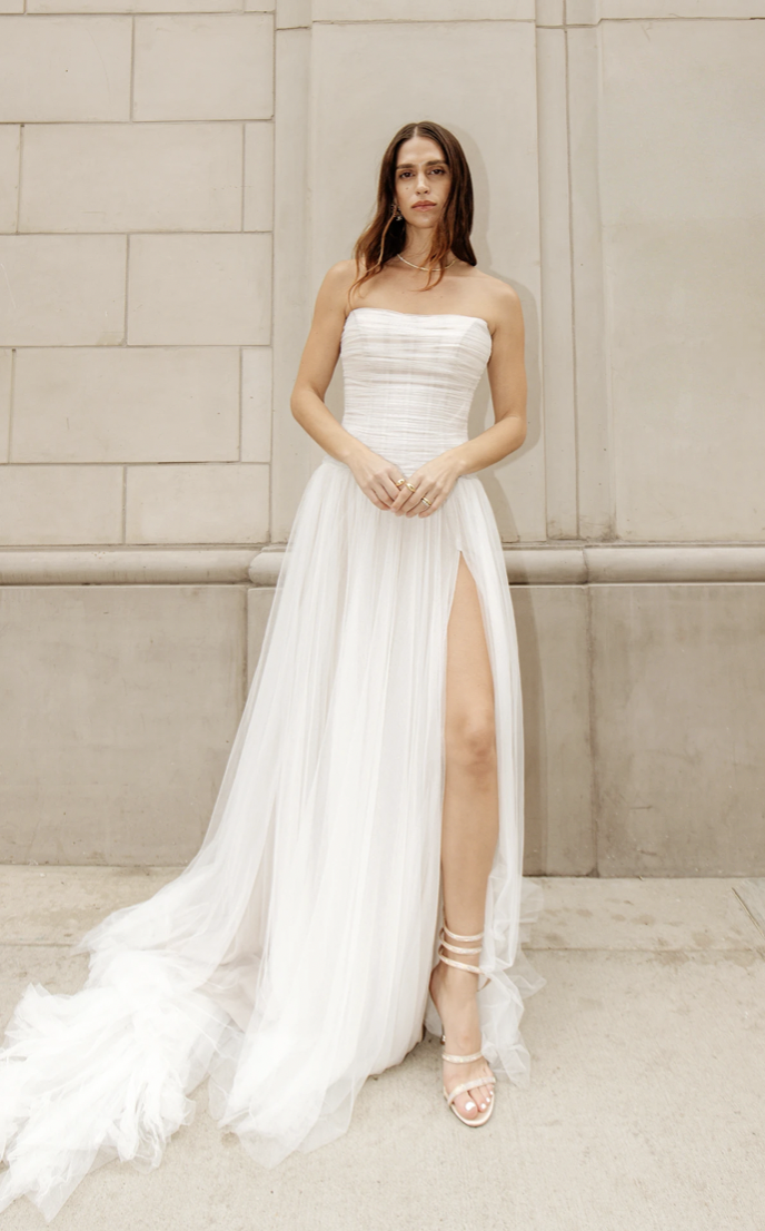 Model is wearing a strapless scoop neck wedding dress with a drop waist